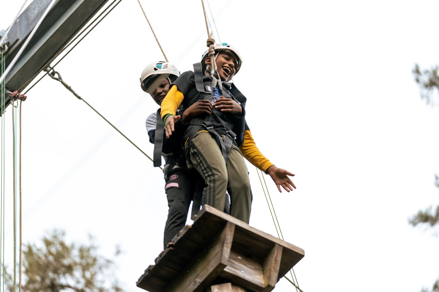 Two Summer Camp participants laughing on a high ropes platform in helmets and harnesses
